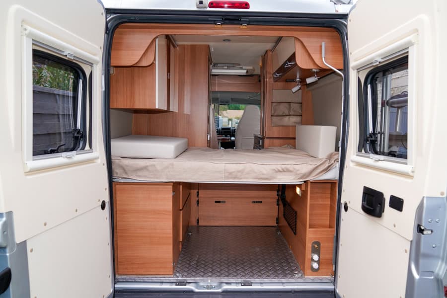 Compact camper van interior with a raised bed, built-in storage cabinets, and under-bed drawers, maximizing space efficiency.