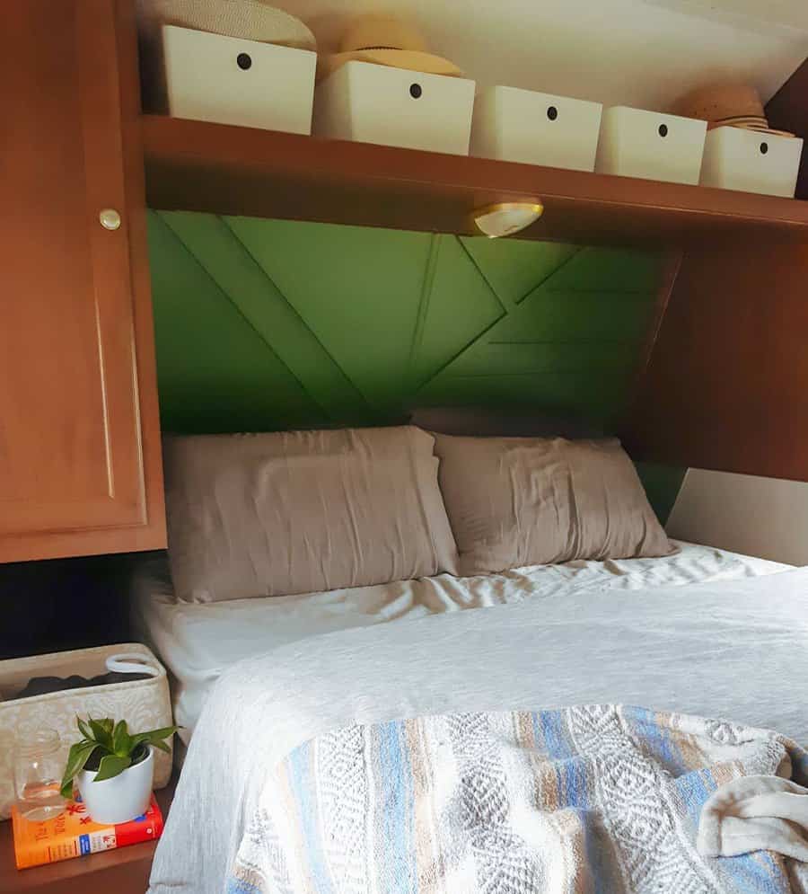 Cozy RV bedroom with overhead storage bins, built-in cabinets, a green accent wall, and a neatly organized bedside area.