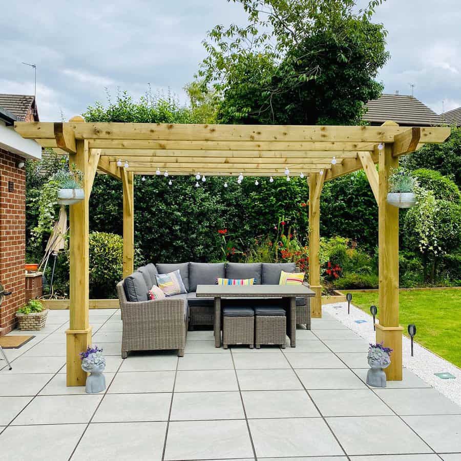 Stylish backyard patio with large square pavers, a wooden pergola, cozy rattan seating, and string lights for a charming outdoor retreat