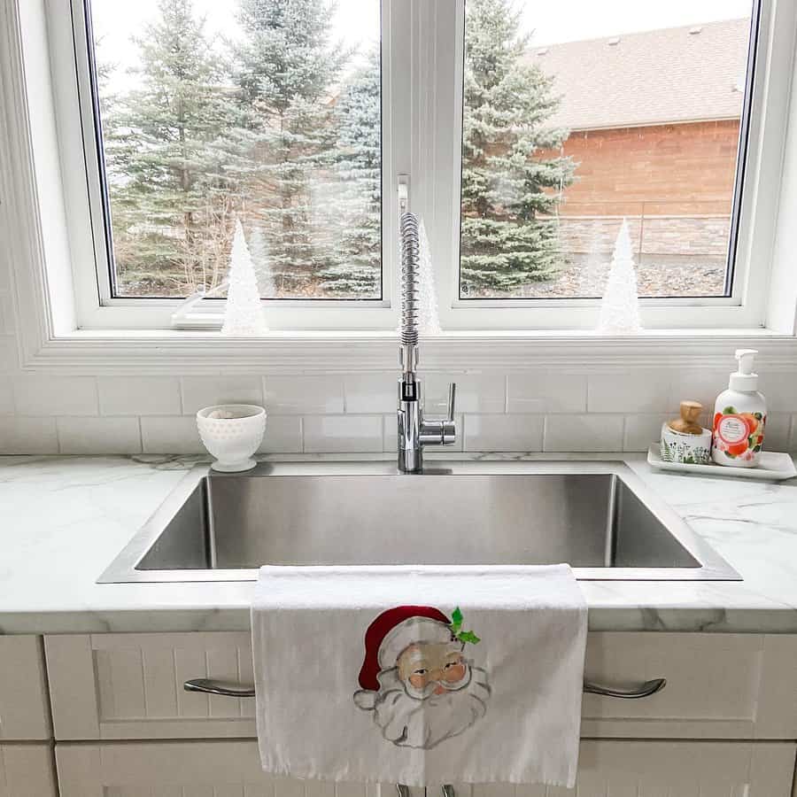 Bright kitchen with a large stainless steel square sink, high-arch spring faucet, marble countertops, and festive holiday decor by the window