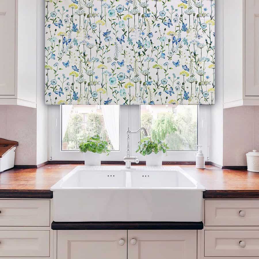 Kitchen with floral patterned Roman shade, white farmhouse sink, wooden countertop, and potted plants by the window