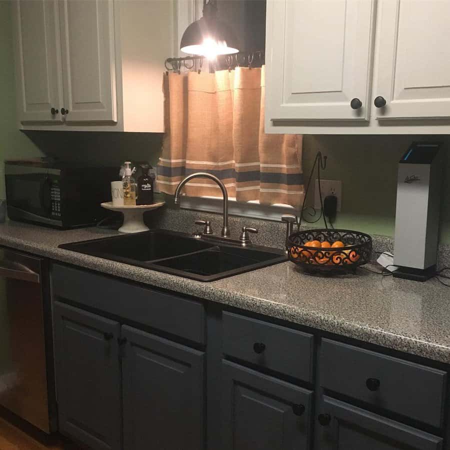 Cozy kitchen with a black double sink, brushed nickel faucet, dark lower cabinets, light upper cabinets, and warm lighting for a rustic feel