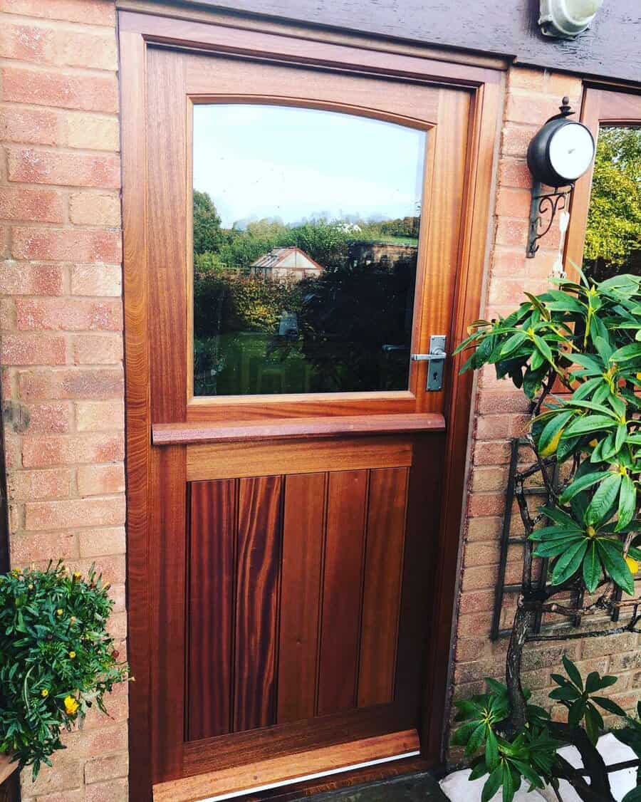 Wooden door with a glass panel set in a brick wall, surrounded by green plants