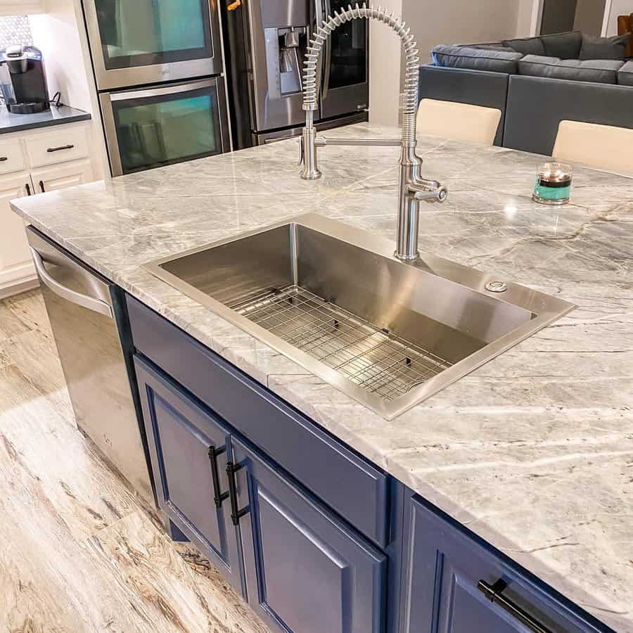 Modern kitchen with blue cabinets, a marble countertop, and a stainless steel sink featuring a tall faucet centered above the sink