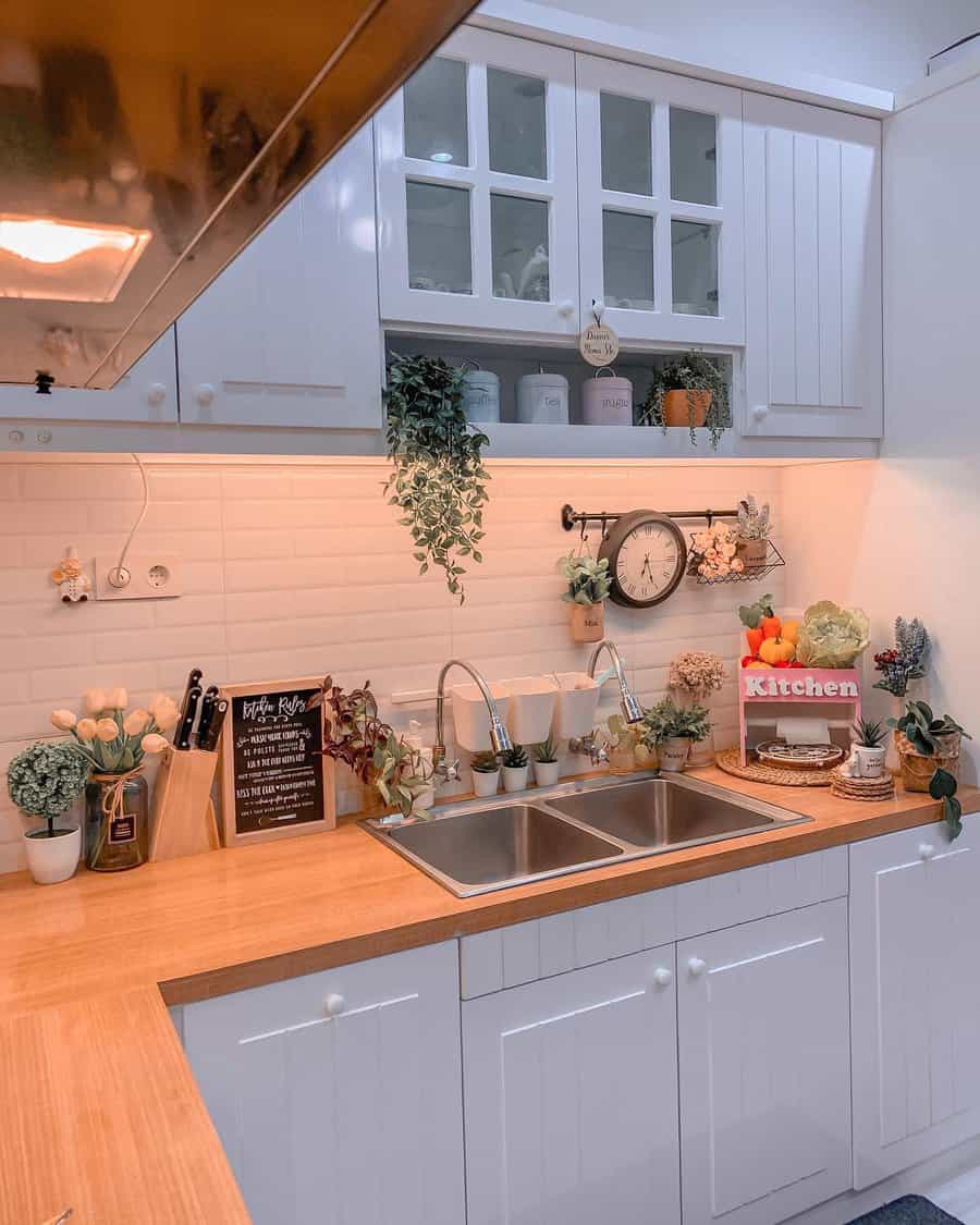 Charming farmhouse kitchen with a stainless steel double sink, wood countertops, white cabinets, and lush greenery for a cozy, inviting feel