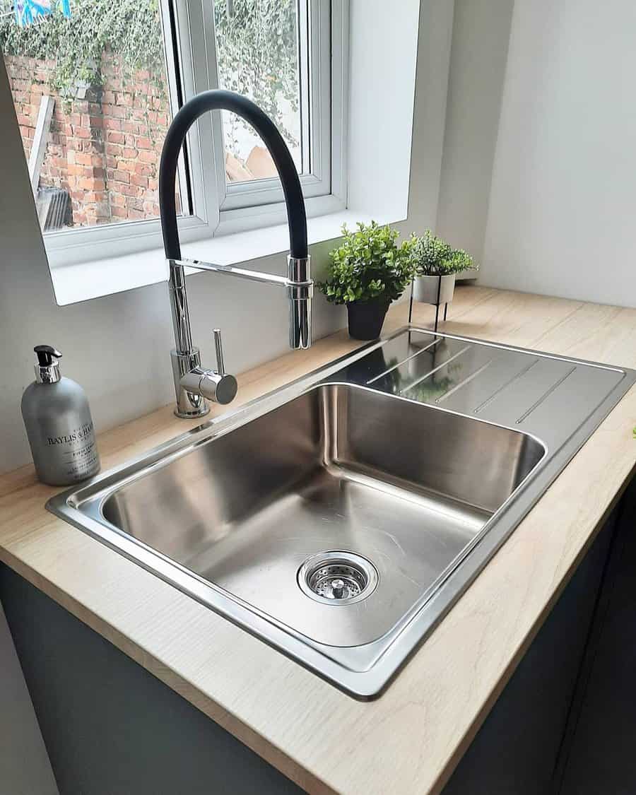 Modern kitchen with a stainless steel sink, built-in drainboard, sleek black high-arch faucet, and wood countertop for a stylish touch