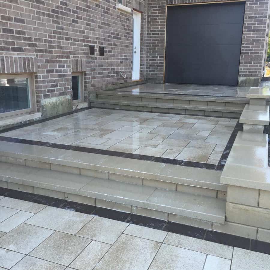 Tiled concrete patio steps by brick house with black trim