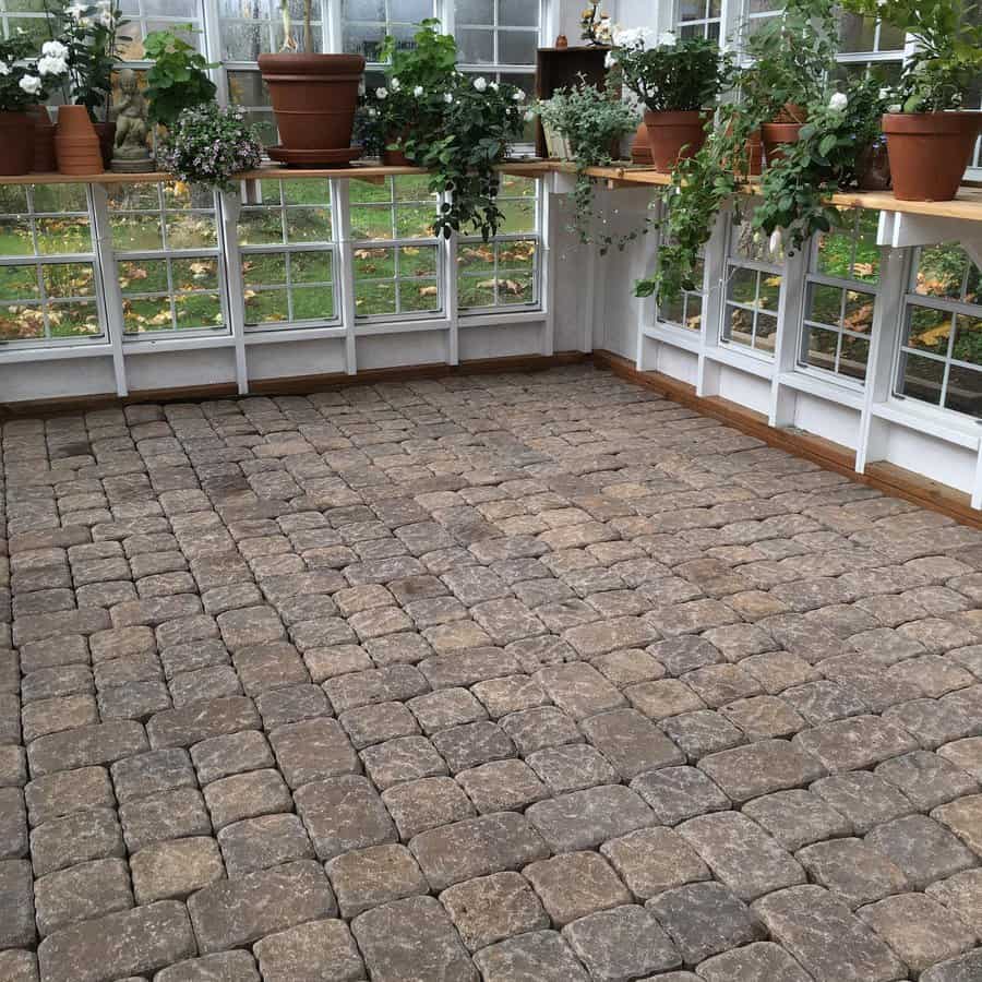 Sunroom with cobblestone floor, potted plants on windowsills, and large windows allowing natural light in