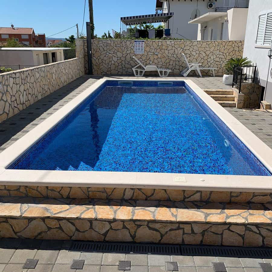 Elegant backyard pool with blue mosaic tiles, stone accents, and lounge chairs, creating a stylish and relaxing outdoor retreat