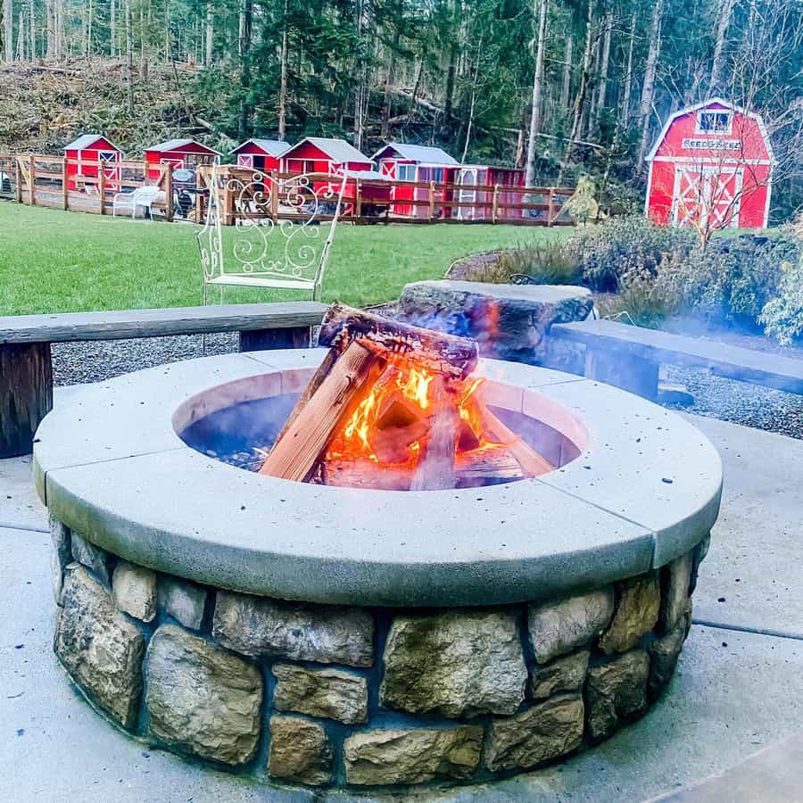 Outdoor stone fire pit with flames, surrounded by brick walls and pavement, in a backyard setting