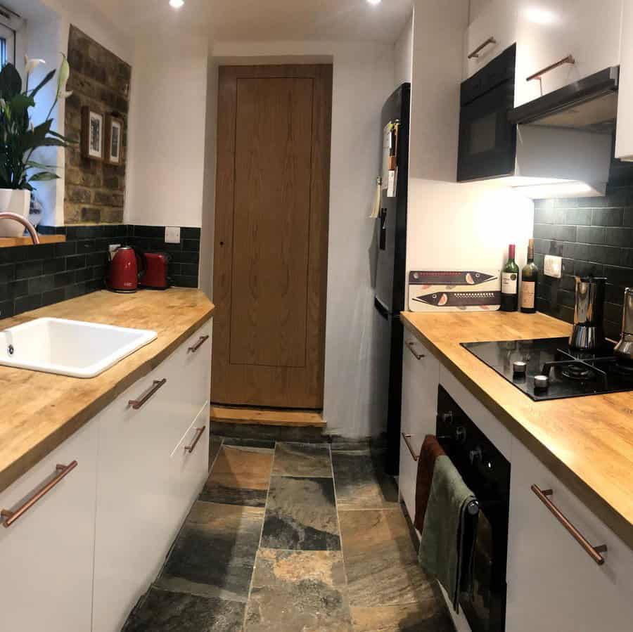 Natural stone flooring adds a rustic charm to this cozy kitchen, complementing wood countertops, white cabinetry, and dark subway tile backsplash