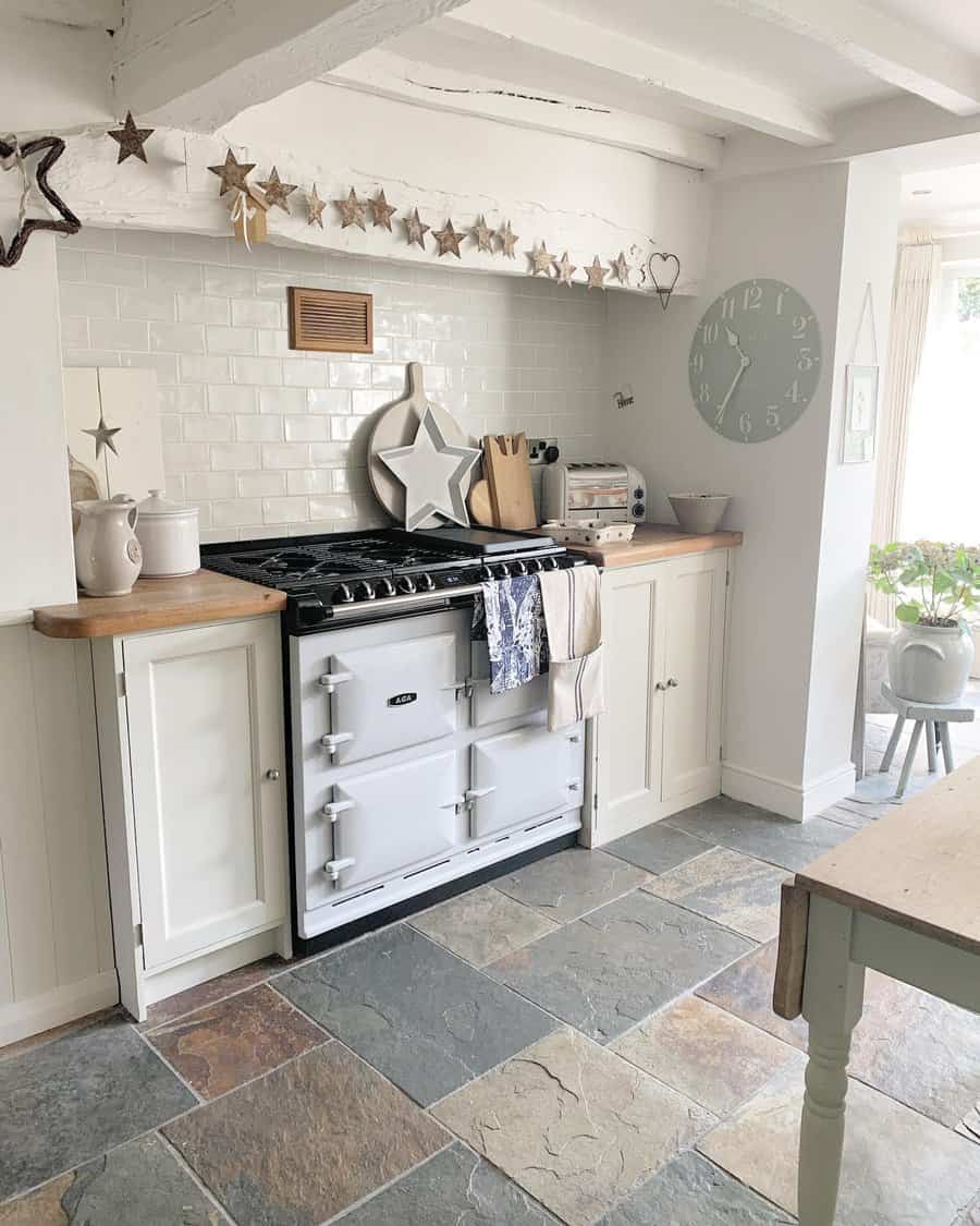 Natural slate flooring adds rustic charm to this cozy farmhouse kitchen, complementing white cabinetry, wooden countertops, and vintage décor