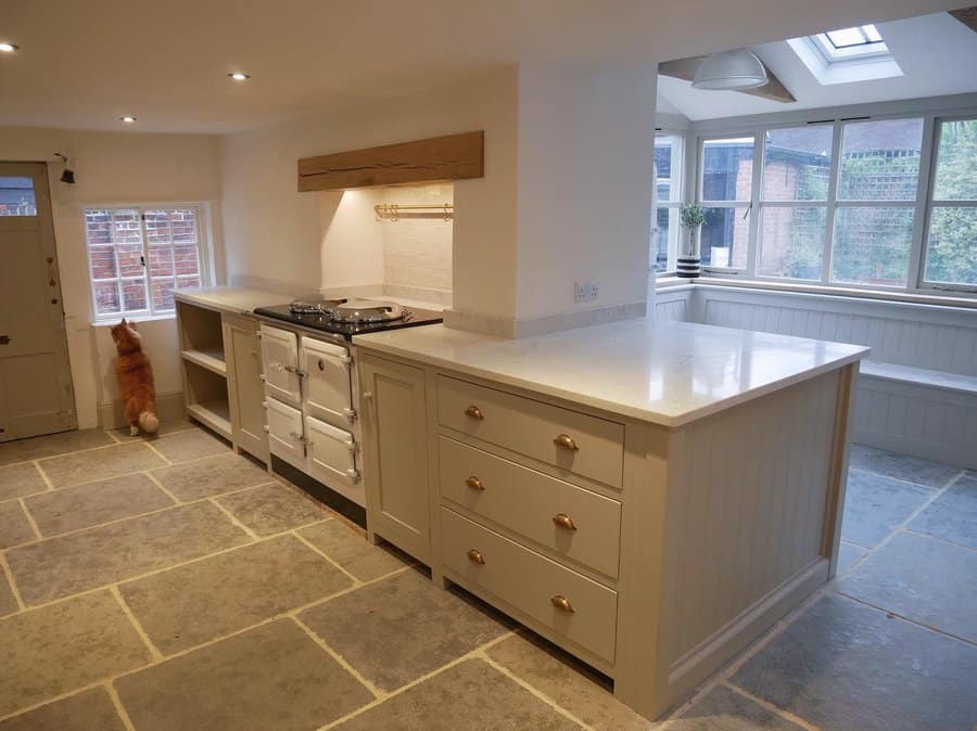 Spacious kitchen with stone tile floor, cream cabinets, and a central island, where a cat peers out the window next to an oven