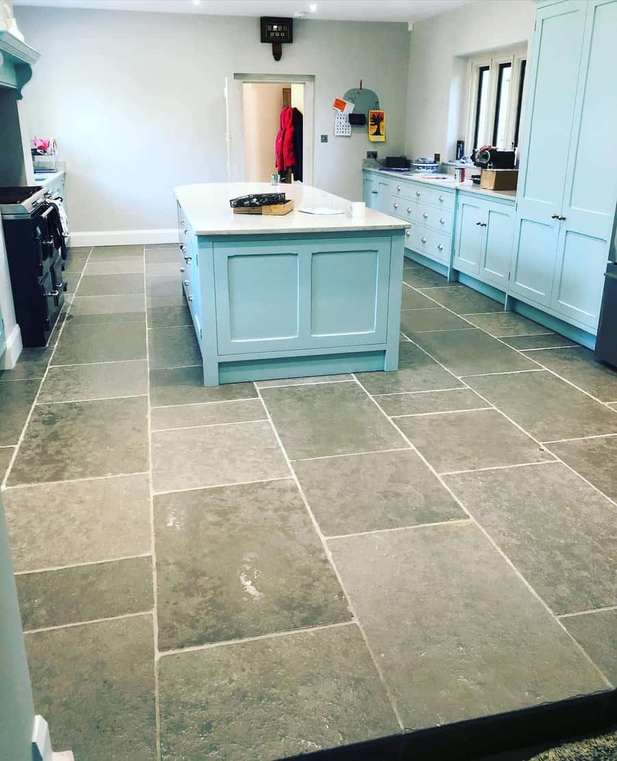 Modern kitchen with large stone tiles, a central island with a white countertop, and pastel blue cabinets creating a bright and spacious ambiance