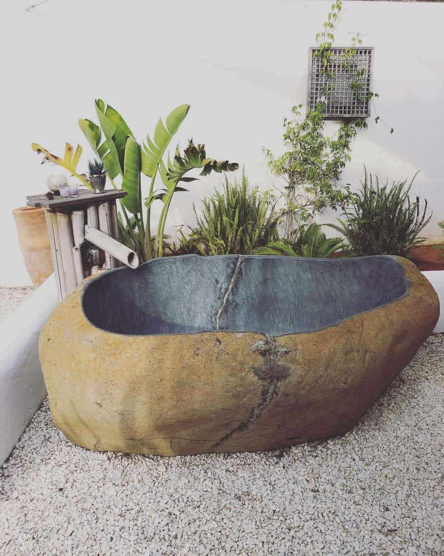 Rustic stone bathtub in a garden setting with tropical plants and bamboo water spout