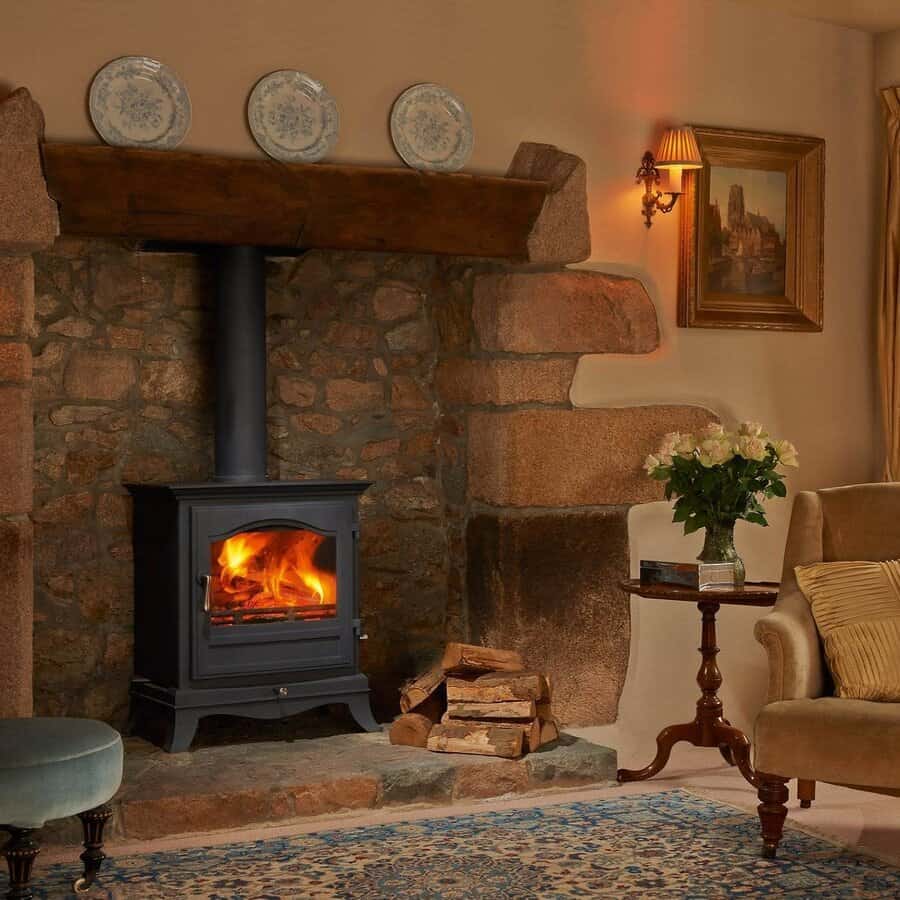 Traditional stone fireplace with a freestanding wood stove, rustic wooden mantel, and warm lighting for a cozy and elegant country-style ambiance.