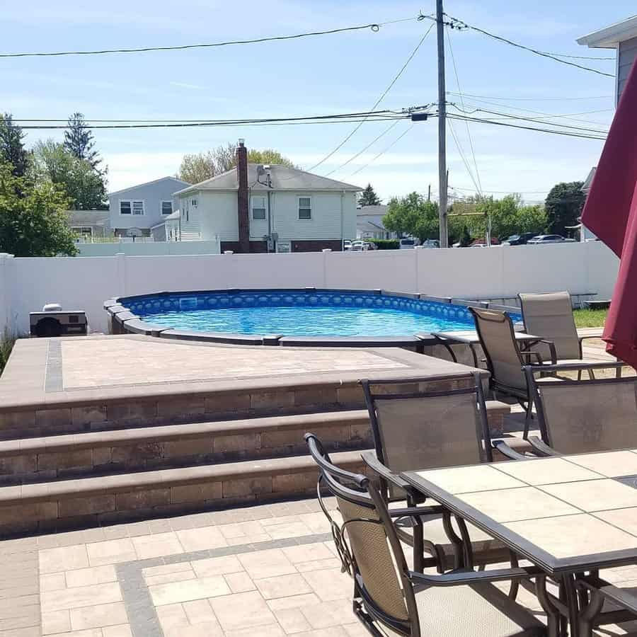 Above-ground pool with a stylish stone patio, built-in steps, and outdoor dining, creating a perfect backyard retreat for relaxation