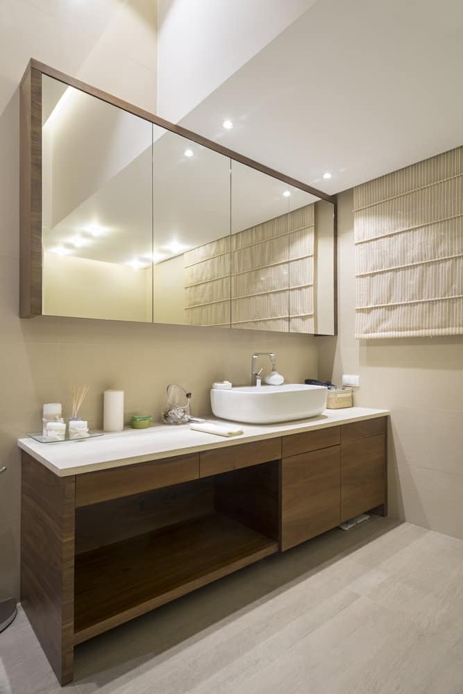 Modern bathroom with a wooden vanity, large mirrors, vessel sink, and soft lighting; beige tones create a warm, inviting atmosphere