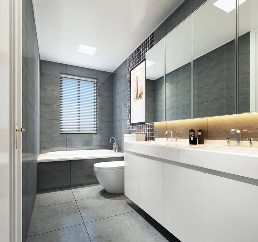 Modern bathroom with gray tiles, white fixtures, a large mirror, a bathtub, and under-cabinet lighting, a window with blinds is visible