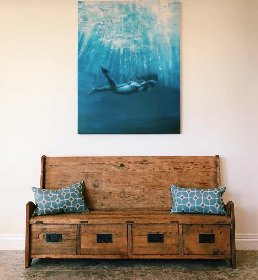 A wooden bench with drawer storage is adorned with patterned pillows, and above, a large painting of a swimmer underwater hangs on the wall