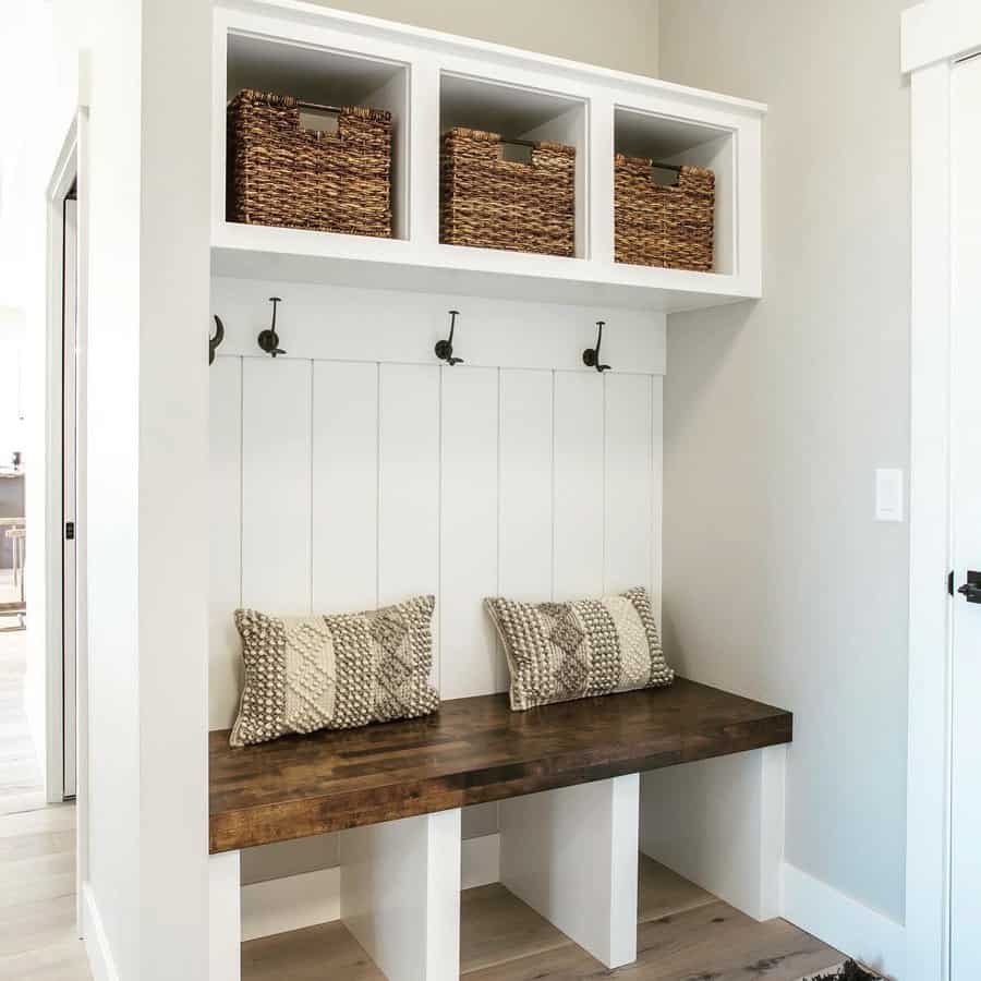 Entryway bench with wooden seat, two patterned cushions, overhead cubbies with woven baskets, and wall hooks for hanging items