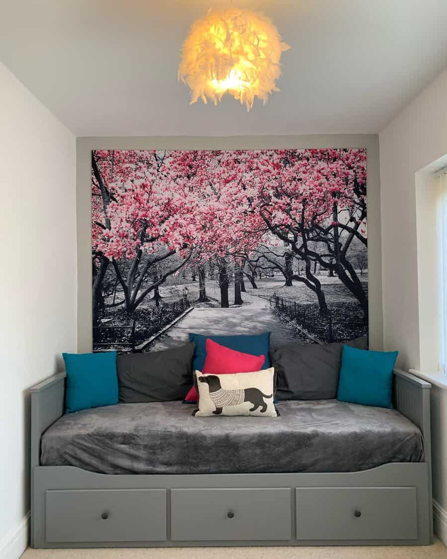 A cozy daybed with blue and gray cushions is beneath a pink cherry blossom wall mural, and a feather-like ceiling light hangs above