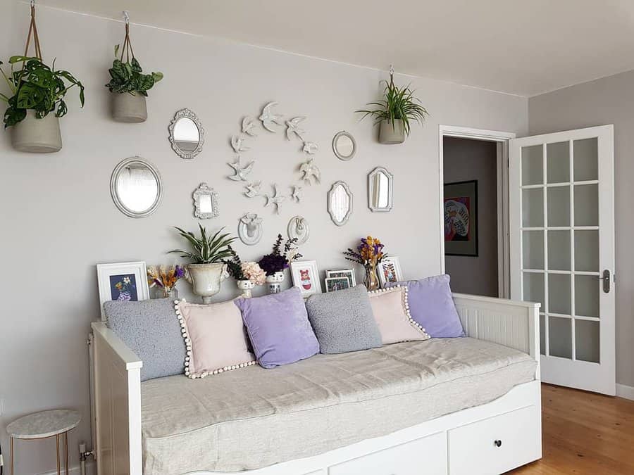 Room with a white daybed, pastel cushions, wall mirrors, and bird decor; hanging plants and a door with glass panes on the right