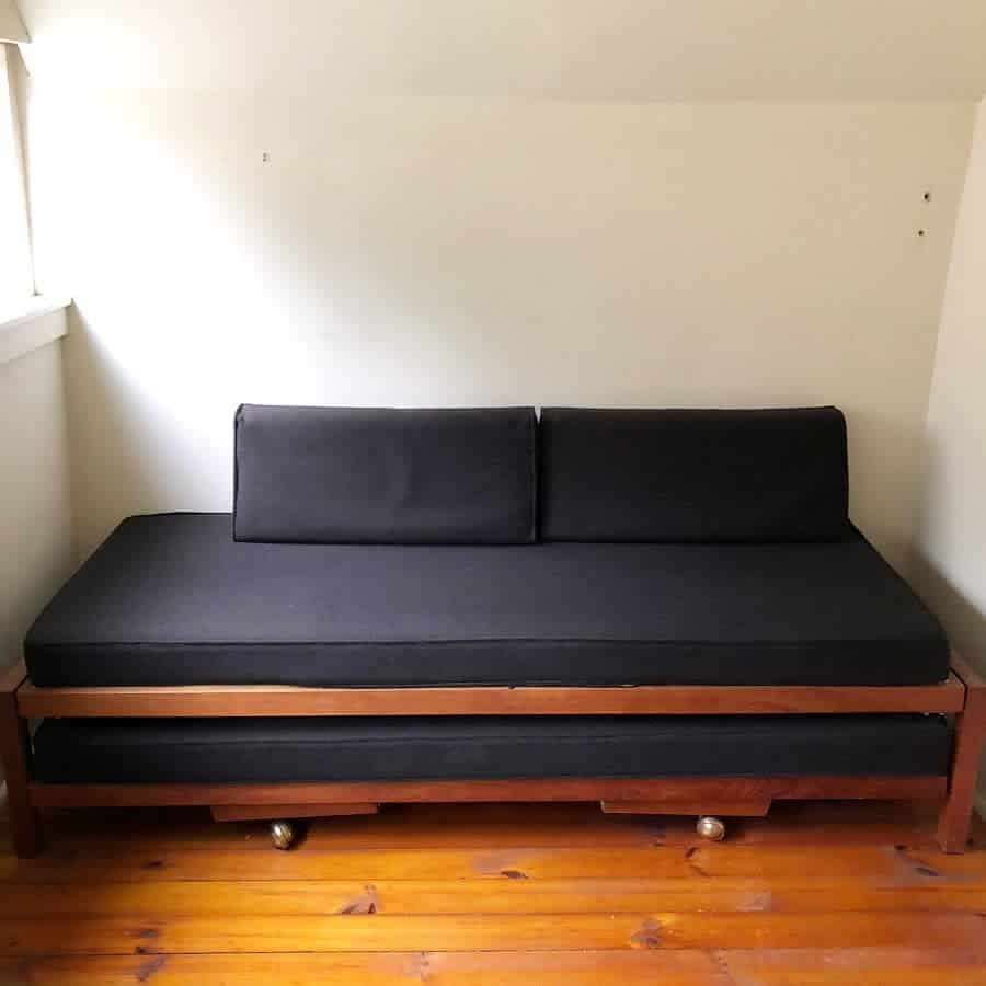 Minimalist wooden trundle daybed with sleek black cushions, offering a space-saving and functional seating and sleeping solution