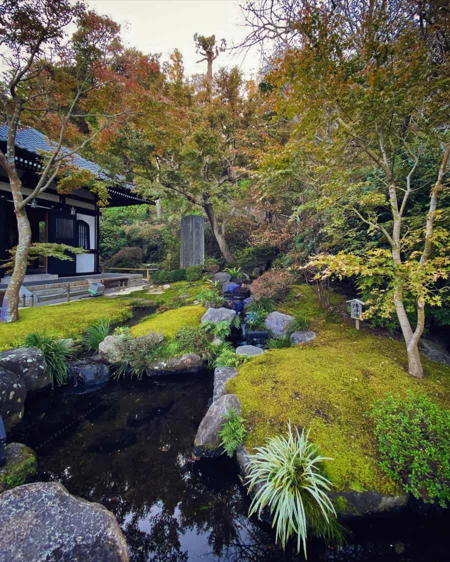 Serene Japanese garden with a moss-covered landscape, small pond, trees with autumn foliage, and a traditional building