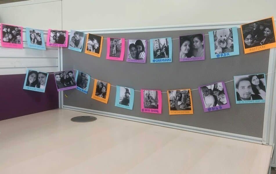 Office cubicle with a bulletin board displaying colorful photo prints of people, each bordered with different colored paper