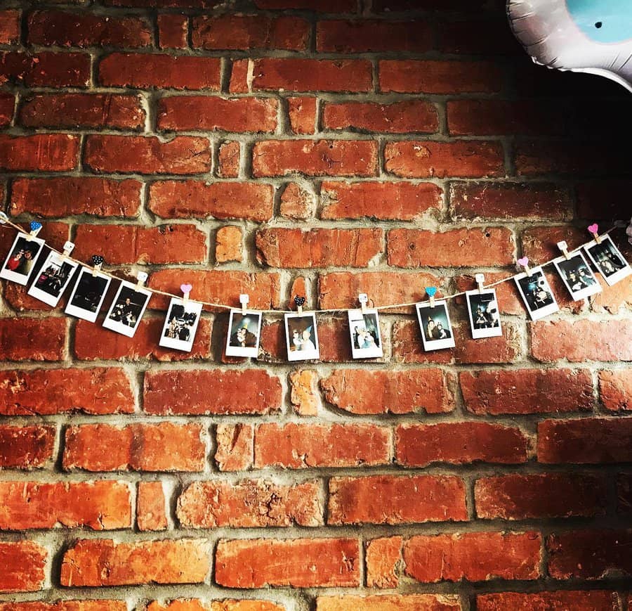 Polaroid photos clipped to a string, hanging on a brick wall, with a part of a balloon visible at the upper right corner