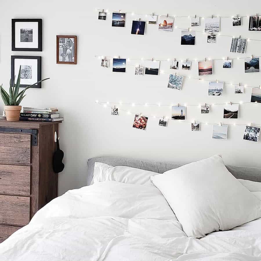 Cozy bedroom with white bedding, a wooden dresser, and a wall decorated with string lights and a collage of photos