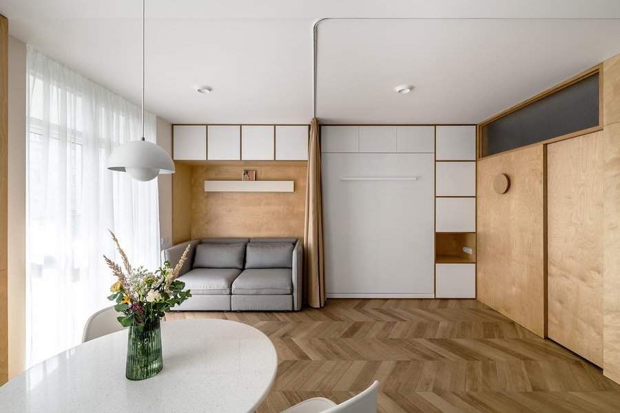 Minimalist studio apartment with built-in storage, a cozy gray sofa, warm wood tones, and natural light creating a sleek and functional living space