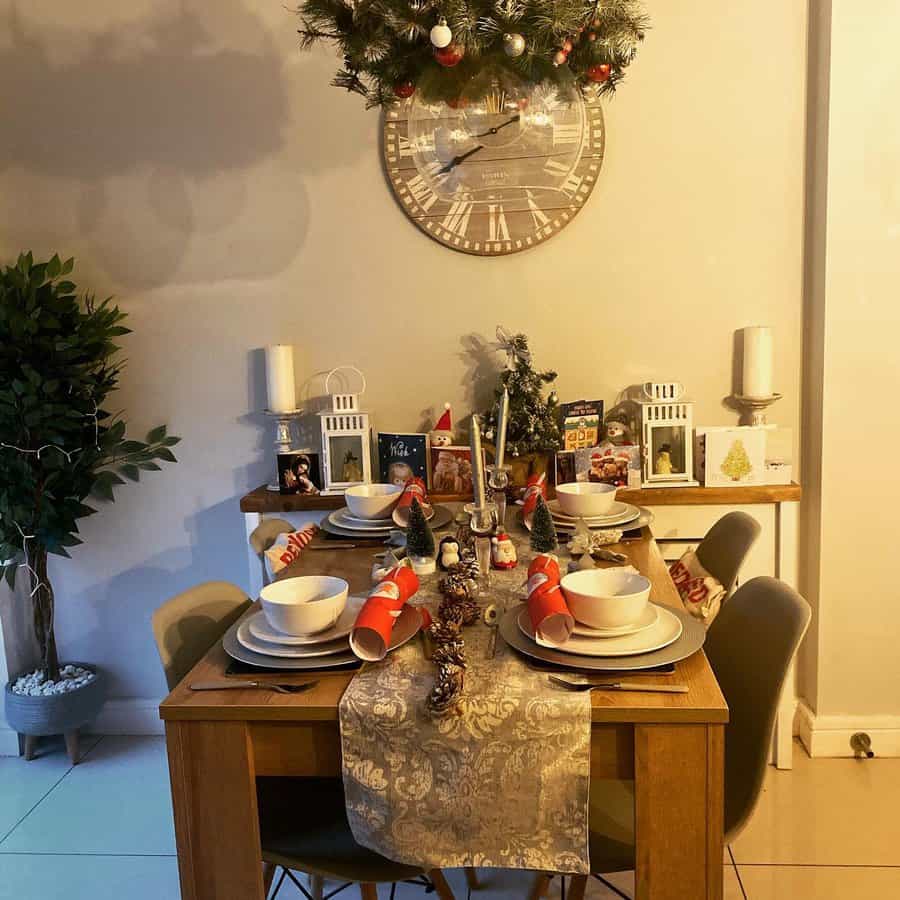 Festive dining table set with Christmas crackers, plates, and candles, hanging greenery and decorative clock in the background