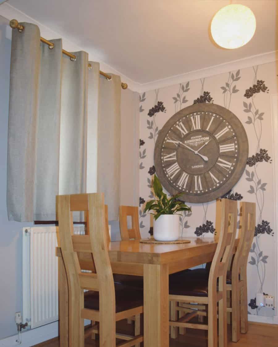 Dining room with a wooden table and chairs, a large wall clock, floral wallpaper, and a potted plant on the table