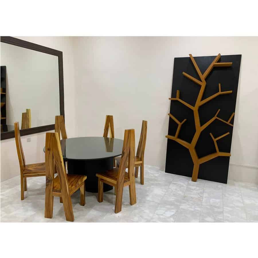 Modern dining area with a round black table, four wooden chairs, and a unique tree-shaped shelf on the wall