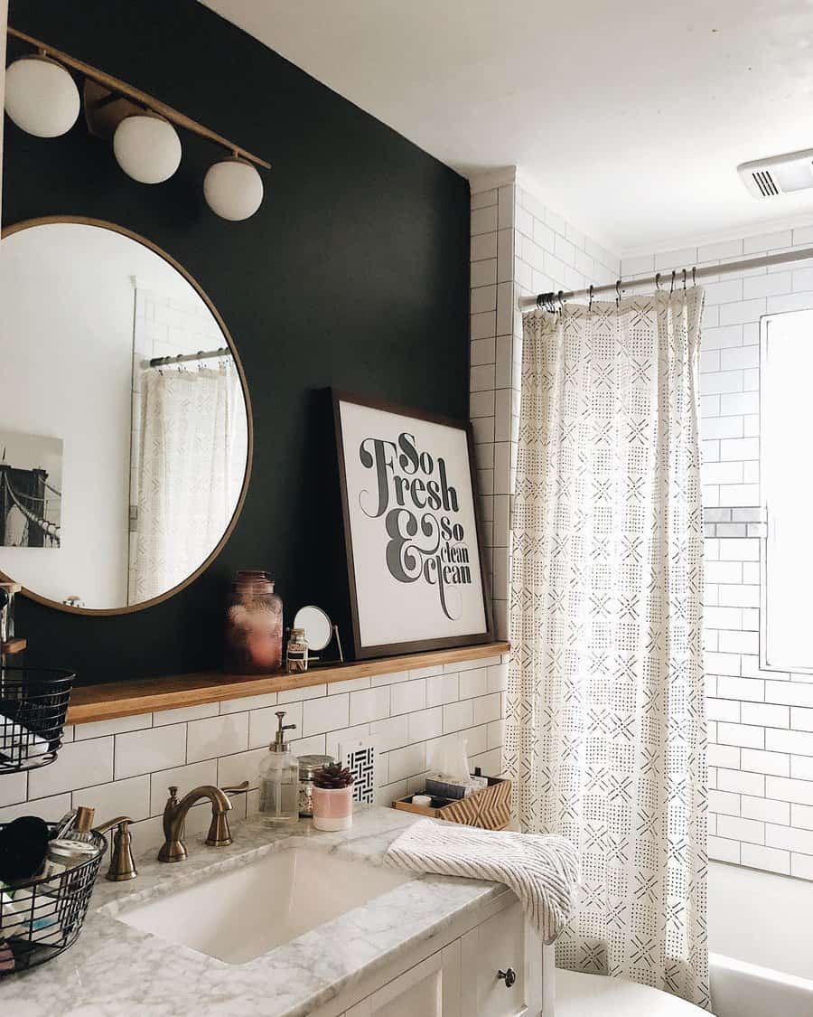 Stylish bathroom with white subway tile backsplash, dark accent wall, round mirror, brass fixtures, and a framed quote on the shelf.