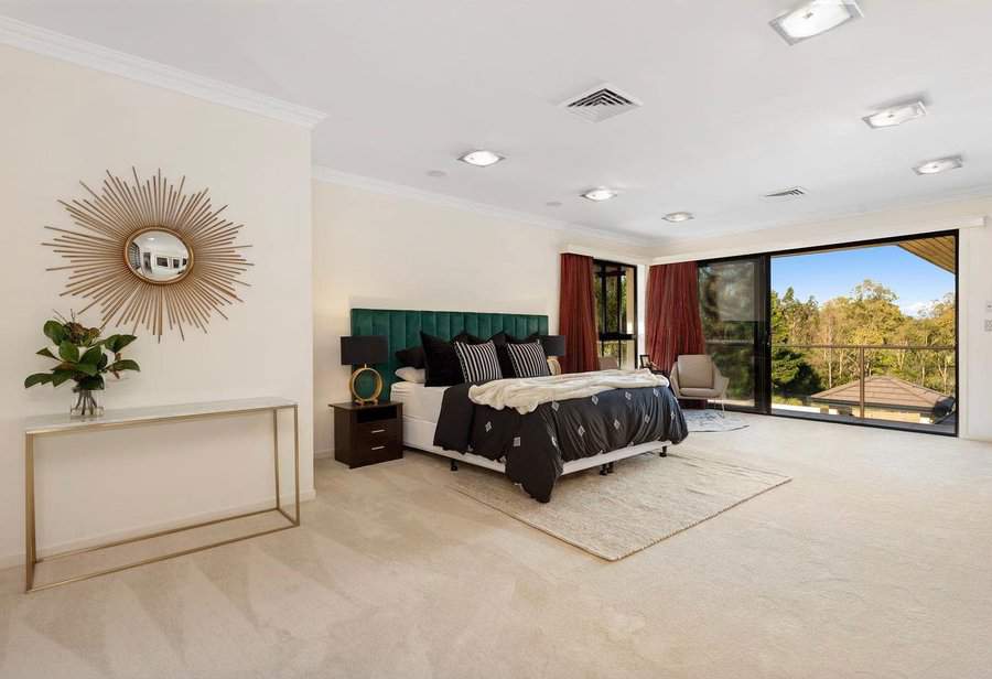 Spacious master bedroom with a large bed, decorative sunburst mirror, modern side table, and floor-to-ceiling windows with a view