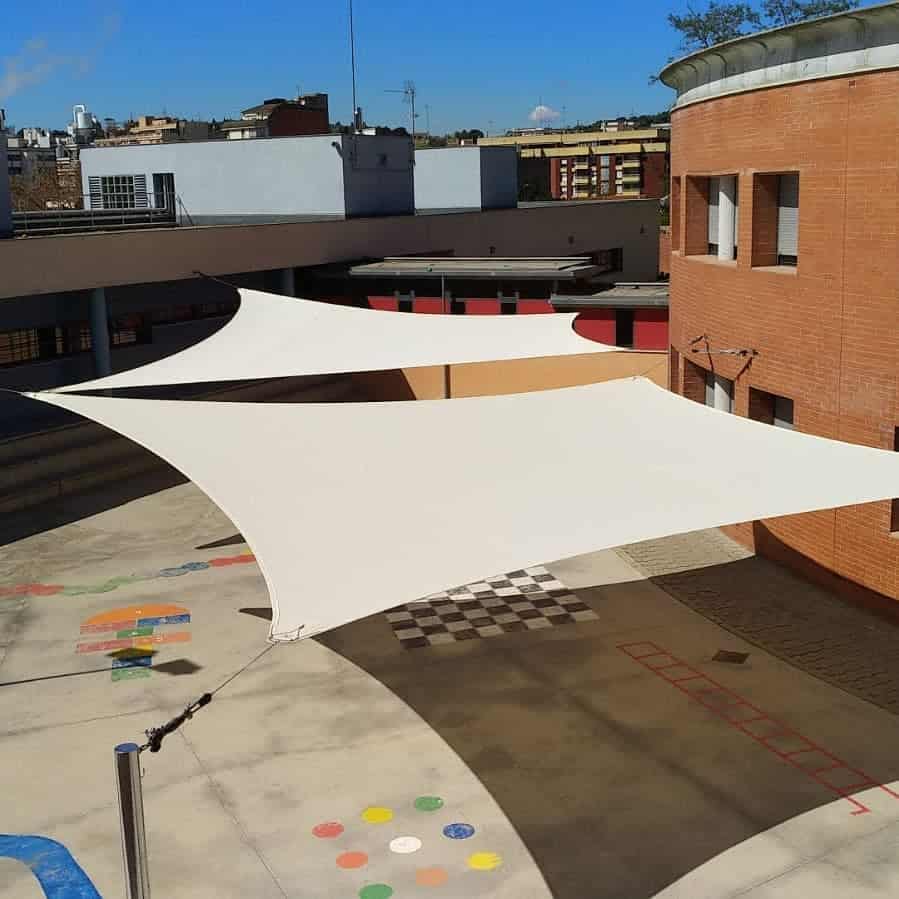 School courtyard with large white shade sails providing sun protection over a colorful playground and activity area