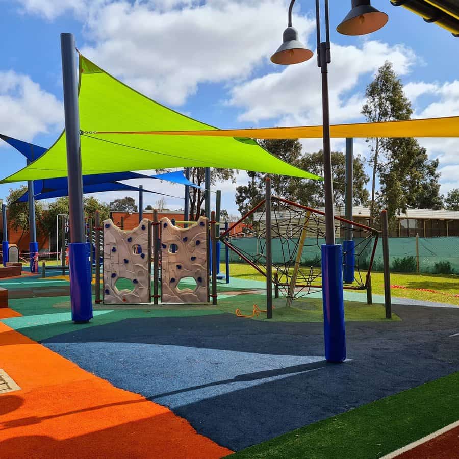 Colorful playground with bright shade sails, soft rubber flooring, climbing structures, and a modern play area for kids