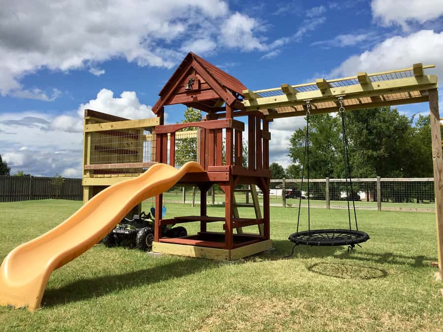 Playground set with wooden climbing frame, slide, and swings in a grassy yard under a partly cloudy sky