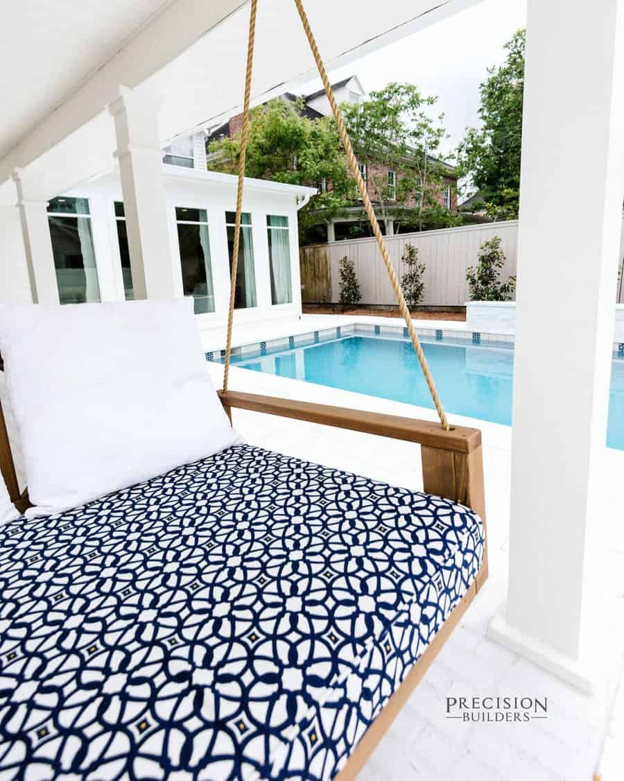 Outdoor patio with a patterned swing daybed, overlooking a clear blue pool, surrounded by white columns and greenery