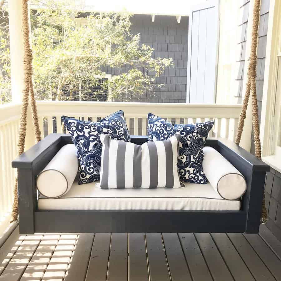 Coastal-style swing daybed with navy blue framing, plush white cushions, and patterned pillows, creating a relaxing and elegant porch retreat