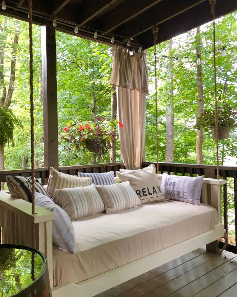 Cozy farmhouse-style swing daybed with neutral cushions, striped pillows, and rope suspension, creating a peaceful outdoor retreat on the porch