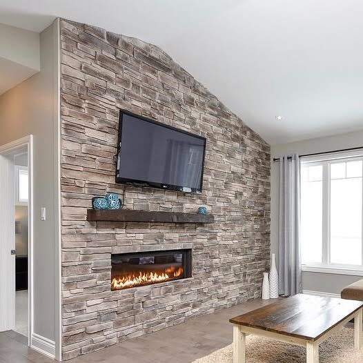 A modern stone fireplace with a sleek, minimalist design, featuring a long, linear fire beneath a wall-mounted TV, creating a contemporary and stylish living space