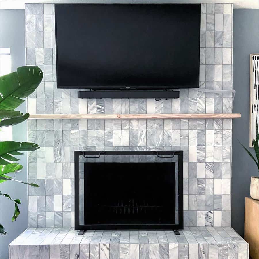 A modern marble-tiled fireplace with a minimalist design, featuring a wall-mounted TV above and a sleek wooden shelf for added elegance