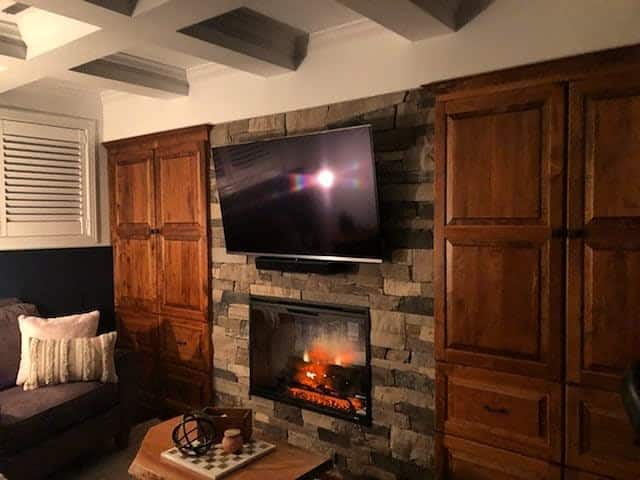 A cozy stone fireplace with a wall-mounted TV above, surrounded by wooden cabinets and a warm ambiance created by a faux fire, making the space inviting and functional