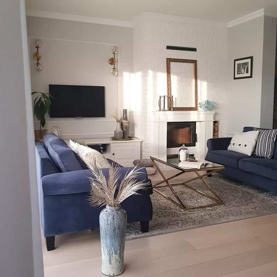 Modern living room with blue sofas, a glass coffee table, and a wall-mounted TV