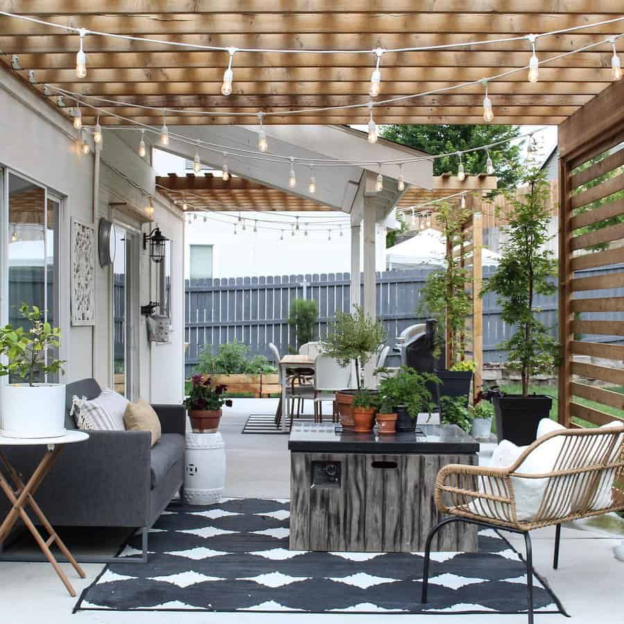 Outdoor patio with seating area, string lights, plants, and patterned rug; cozy and inviting space with modern and rustic elements