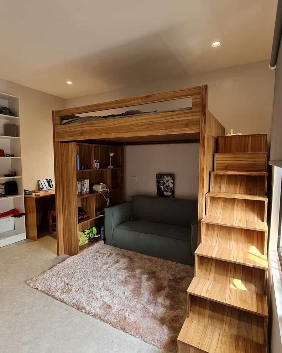 Wooden loft bed with under-bed couch and side staircase, built-in bookshelves and a desk with items in the corner, cream rug on floor